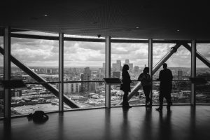 Three people looking out a massive glass window high up, like 360 degree feedback gives a view of everything in scope