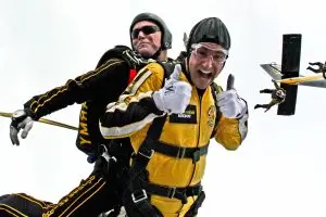 Two people strapped together jumping out a plane with a parachute they share - helping each others success